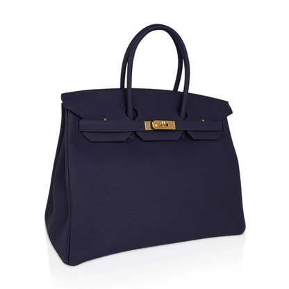 Saturated Midnight Navy Soft Subtle Pebbled Grain Roomy Structured Hand Tote With Seamless Uniform Stitching, Polished Golden Twist Lock Hardware And Matching Suspended Textured Tag Striped Metal Padlock Charm